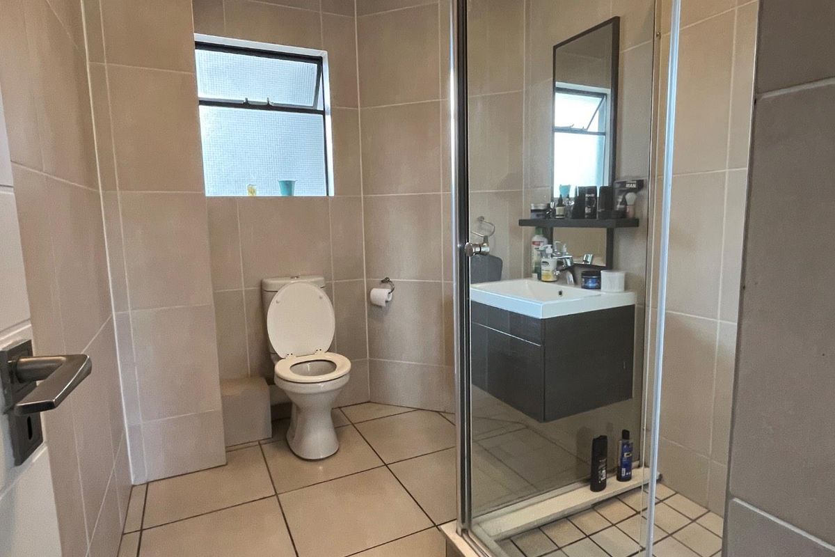A modern bathroom featuring floor-to-ceiling neutral tiling, a glass-enclosed shower, a wall-mounted vanity with basin, and a standard toilet.