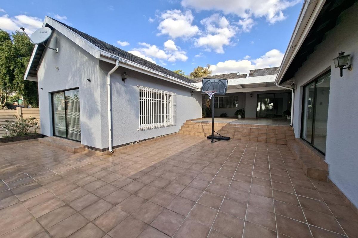 Spacious rear tiled patio area featuring sliding glass doors, security bars, and integrated outdoor lighting, providing a functional space for outdoor living.