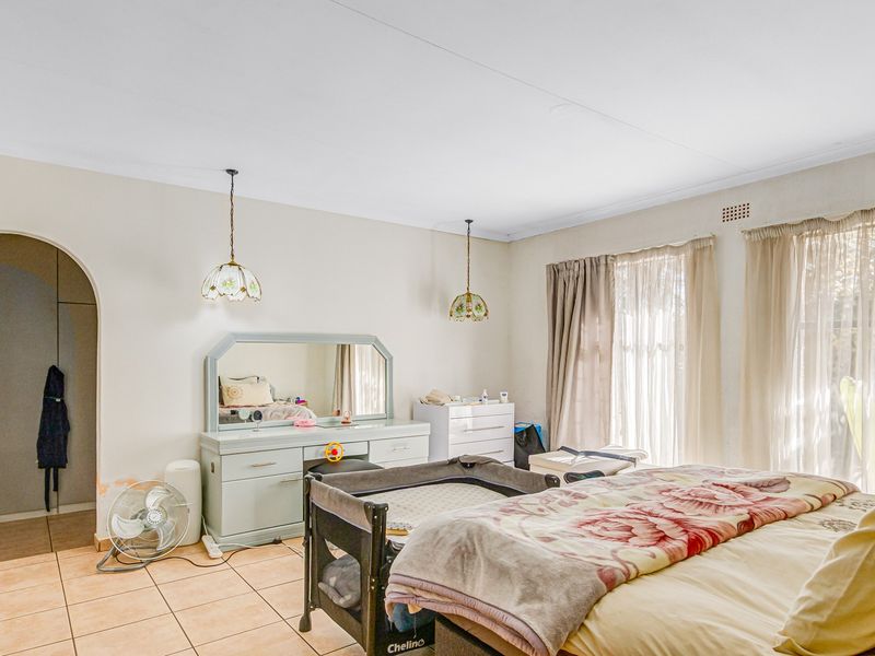 Spacious bedroom featuring tiled flooring, an arched entryway, and classic pendant lighting, offering a functional layout ready for cosmetic updates.