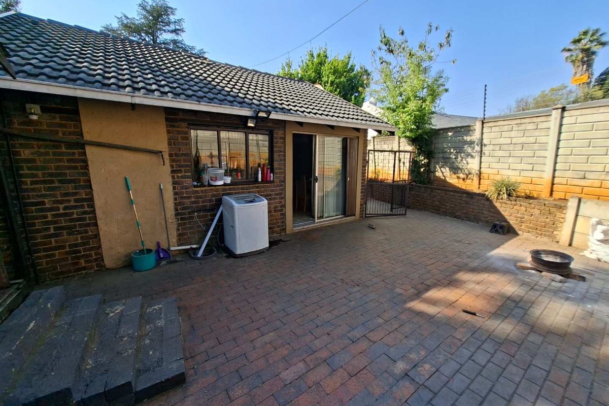 Rear exterior view of the property featuring a paved patio area, brick boundary walls, and direct access via a sliding glass door.