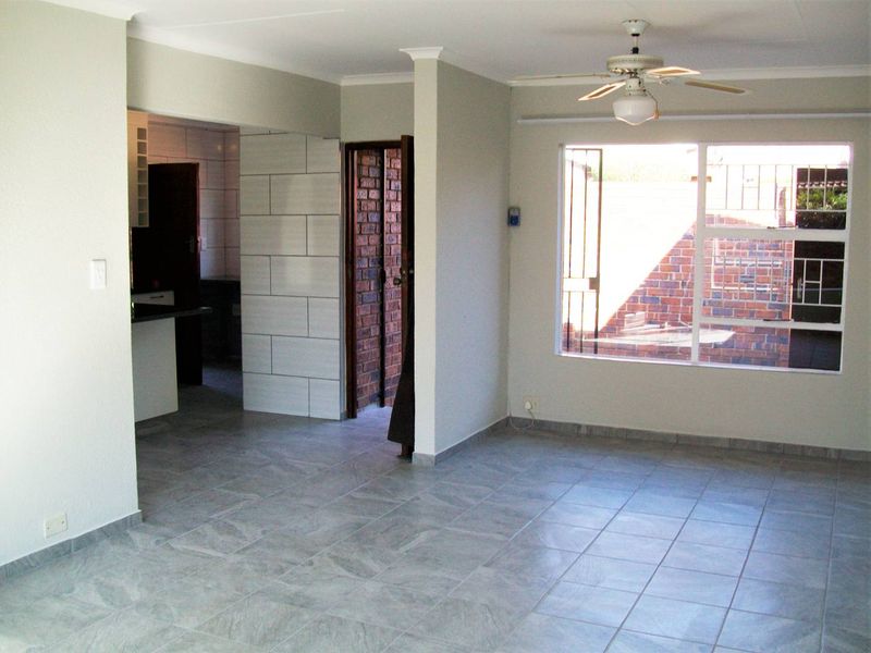 An open-plan living area featuring neutral tiled flooring, a ceiling fan, and direct access to an adjacent kitchen and exterior space.