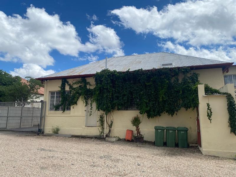 Rear exterior view of the property featuring a corrugated metal roof, security bars on windows, and a gravel driveway area.