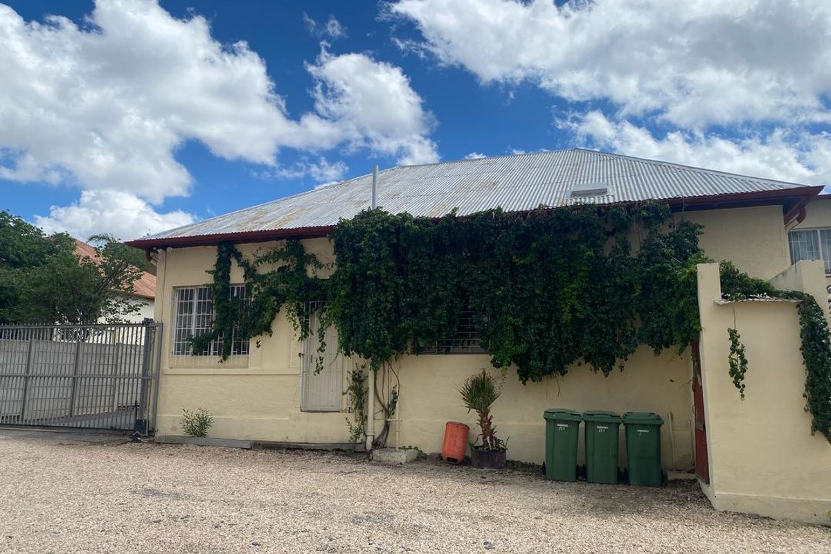 Rear exterior view of the property featuring a corrugated metal roof, security bars on windows, and a gravel driveway area.