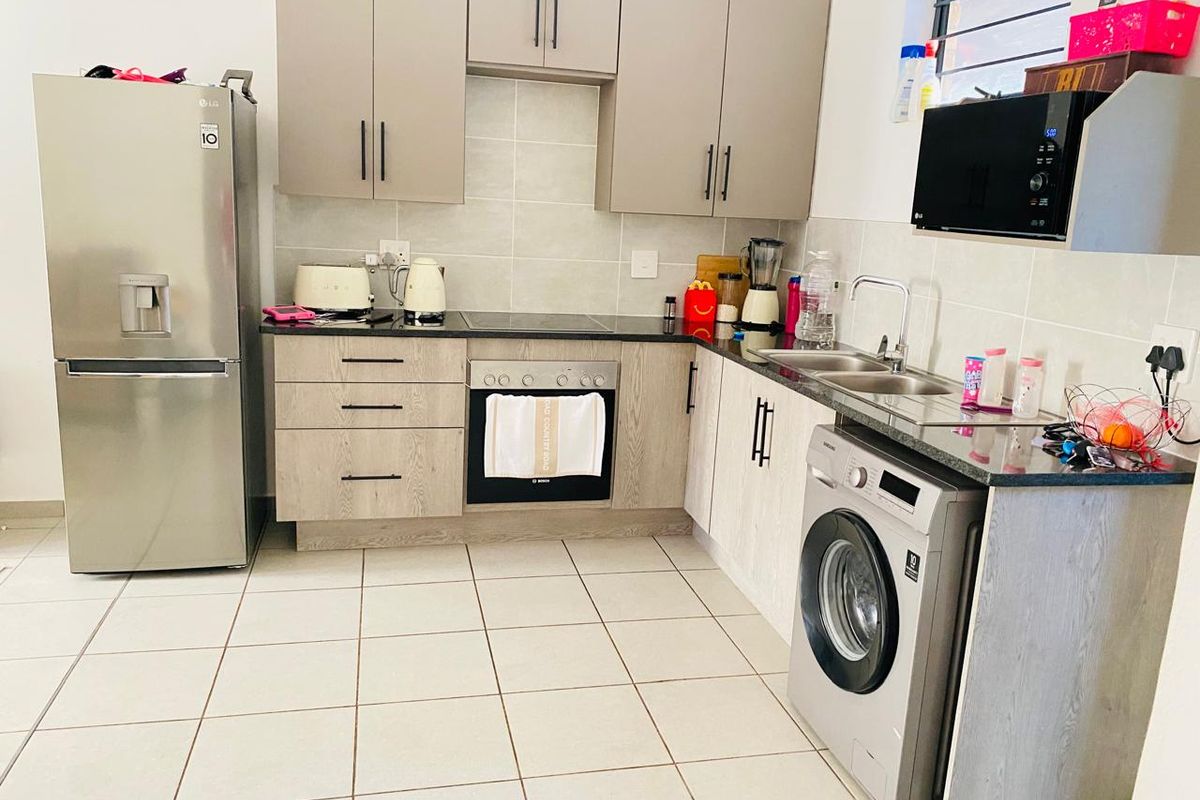 A functional kitchen featuring modern light-wood cabinetry, granite countertops, a built-in oven, electric hob, and tiled flooring with integrated laundry plumbing.