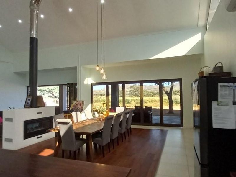 Spacious open-plan living and dining area featuring a modern freestanding fireplace, vaulted ceilings, timber flooring, and large sliding doors opening to scenic views.