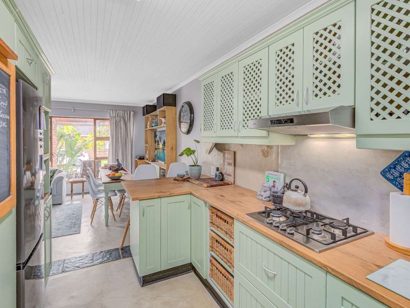 Open-plan kitchen featuring light green cabinetry, wooden countertops, a built-in gas hob, and an extractor fan, flowing into a dining and living area.
