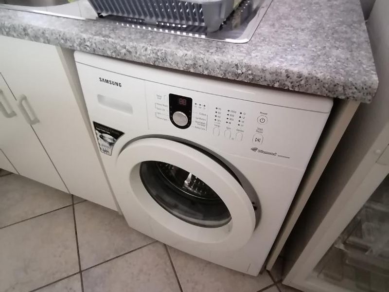 A functional laundry area featuring a built-in sink, tiled backsplash, and space for a front-loading washing machine with tiled flooring.