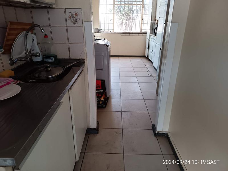 A functional kitchen area featuring built-in cabinetry, a stainless steel sink, and tiled flooring, requiring cosmetic updates to modernize the space.