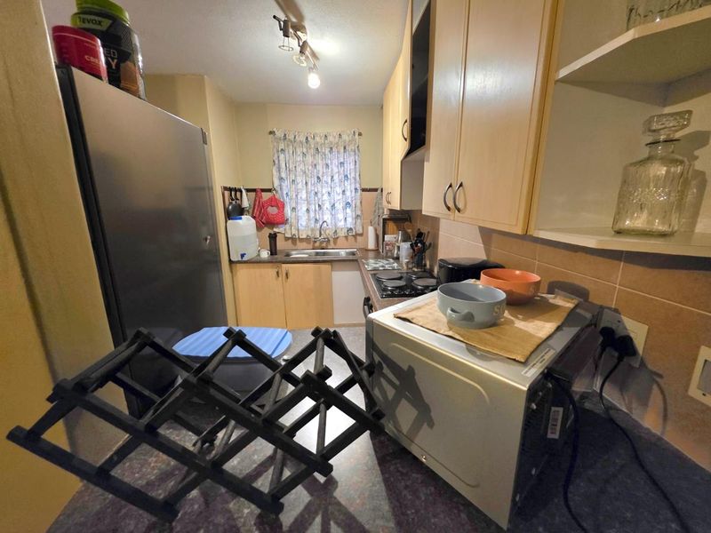A functional kitchen featuring laminate cabinetry, a tiled backsplash, and an electric hob, offering a practical layout for daily meal preparation.