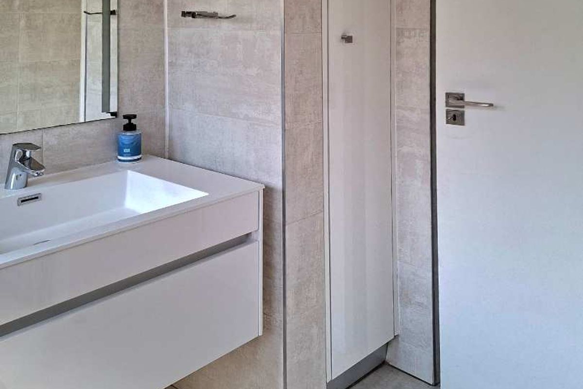 Modern bathroom featuring a wall-mounted vanity with integrated basin, neutral tiled walls and flooring, and a built-in storage cupboard.