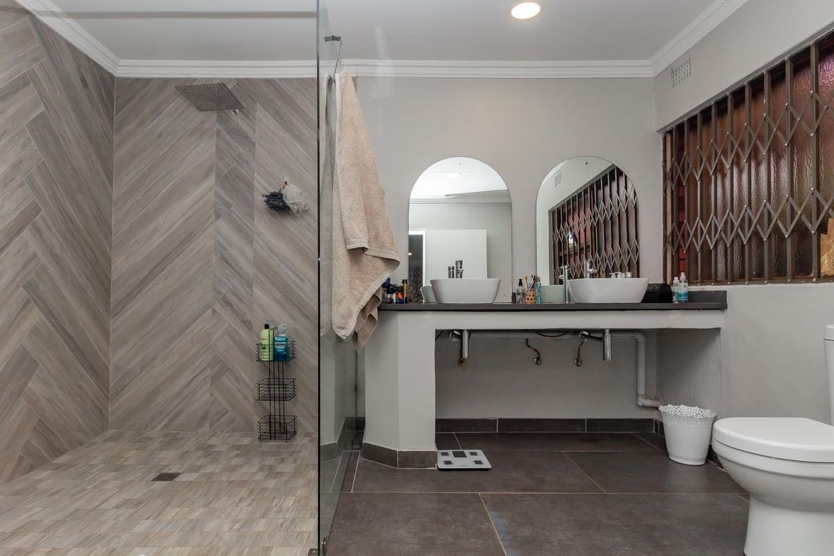 Modern bathroom featuring a spacious walk-in shower with herringbone tile detail, dual vessel sinks on a concrete vanity, and a private toilet area.