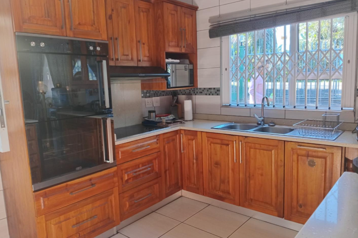 A functional kitchen featuring solid wood cabinetry, a built-in oven, a ceramic hob, and a double-basin sink with a window view.