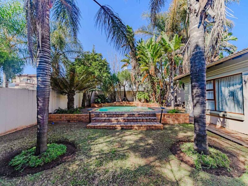 A private backyard featuring a raised swimming pool with brick surround, steps, and established garden landscaping.