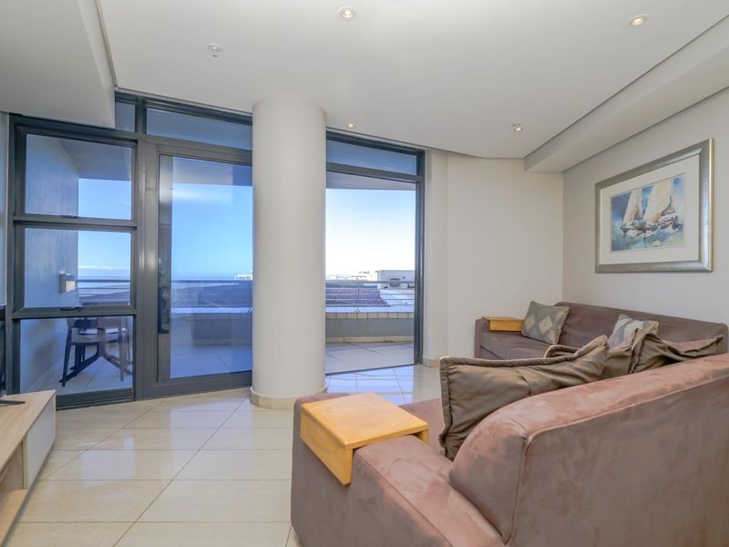 A bright, modern living room featuring large sliding glass doors that open onto a balcony, tiled floors, and recessed ceiling lighting.