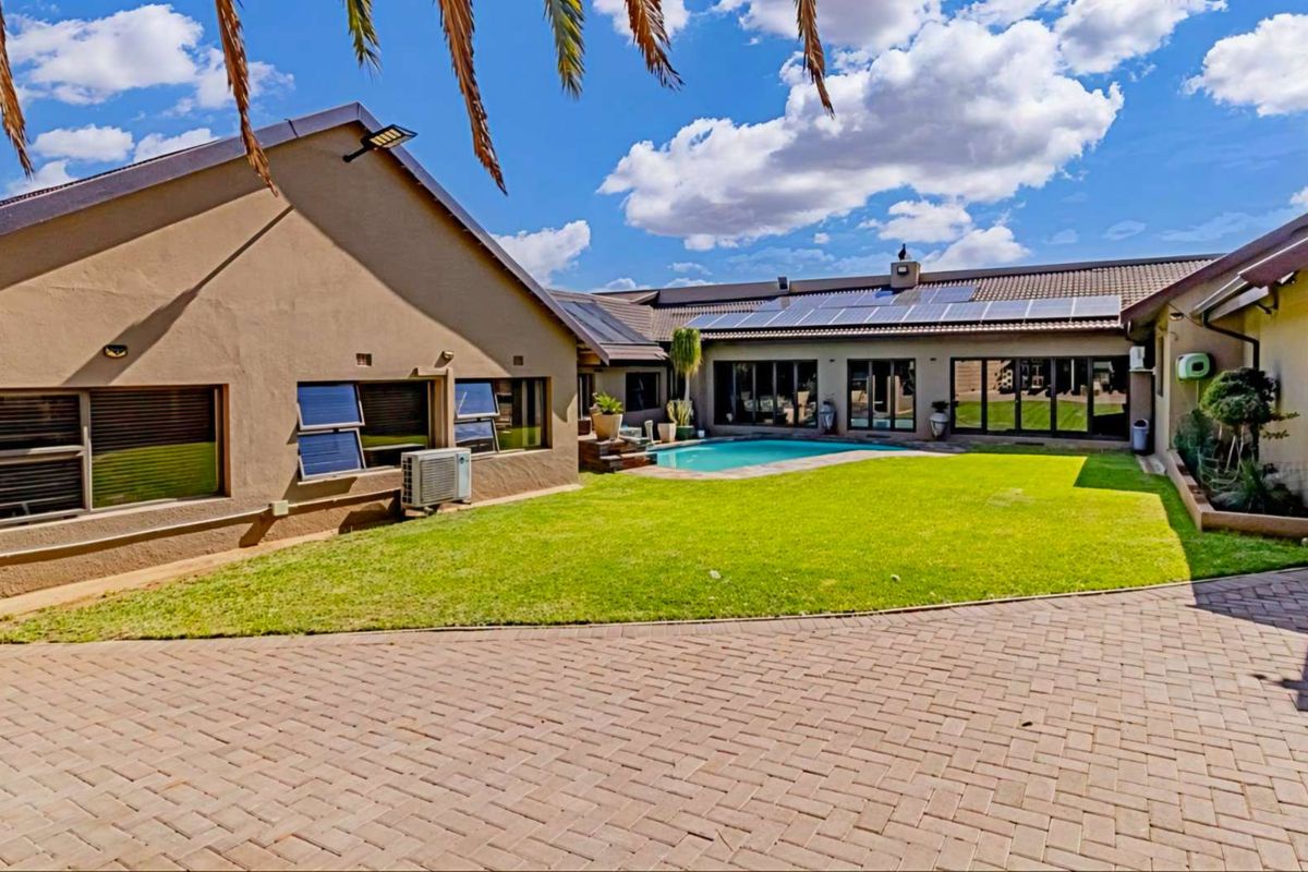 Spacious rear exterior featuring a well-maintained lawn, swimming pool, paved courtyard area, and roof-mounted solar panels.
