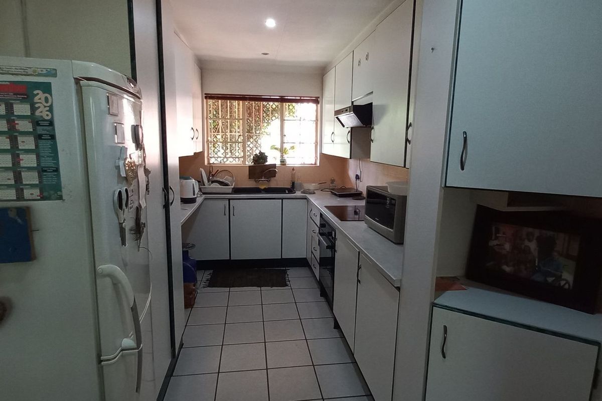 A functional galley-style kitchen featuring white cabinetry, tiled flooring, and a window providing natural light over the sink area.