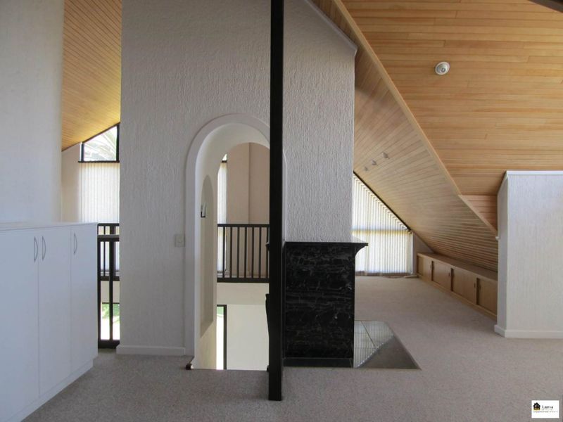 Spacious loft-style living area featuring a vaulted timber ceiling, built-in storage, and a central marble-faced fireplace with an arched architectural transition.