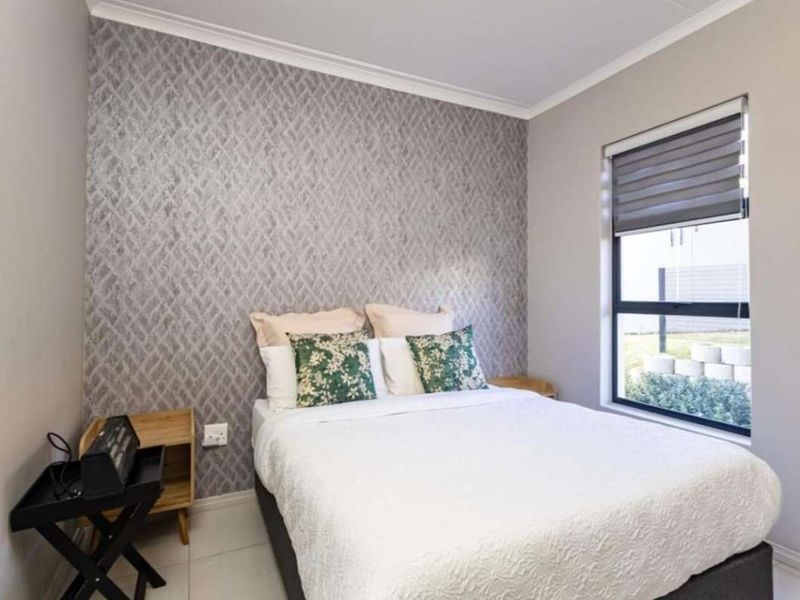 A well-maintained bedroom featuring a decorative textured feature wall, neutral tiled flooring, and a window fitted with a modern roller blind.
