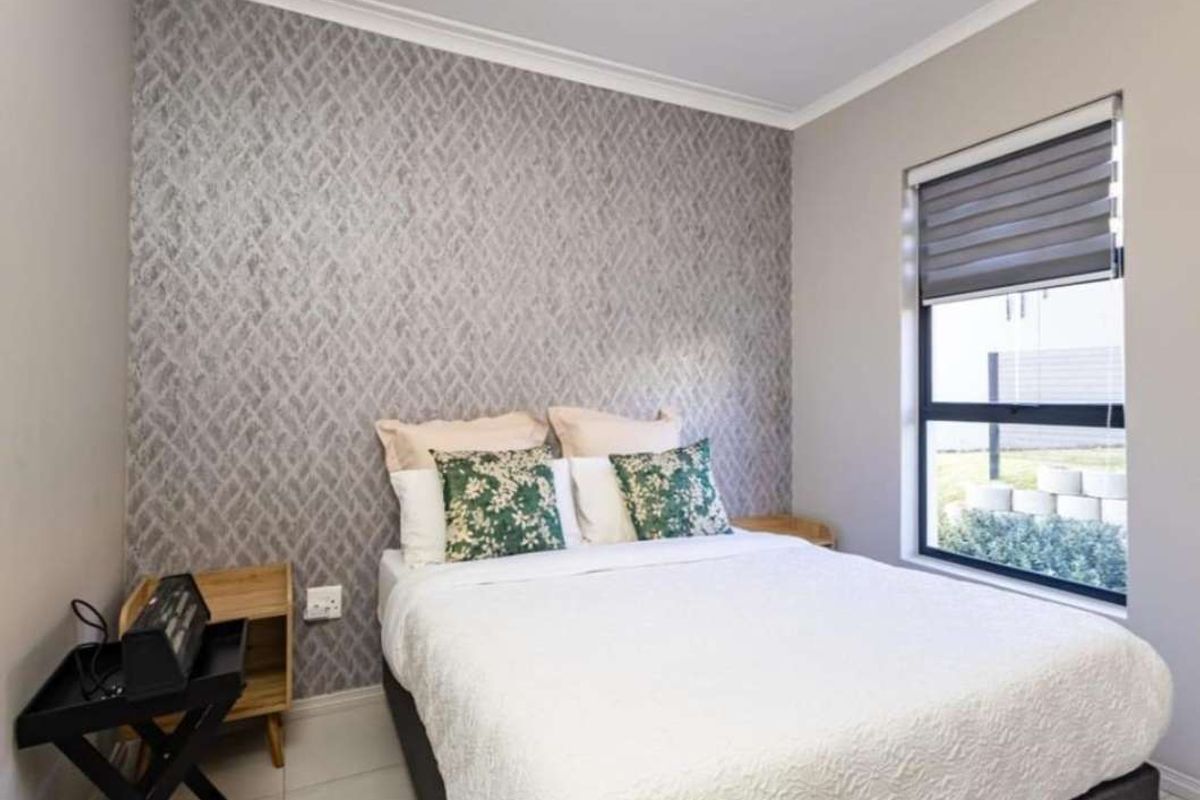 A well-maintained bedroom featuring a decorative textured feature wall, neutral tiled flooring, and a window fitted with a modern roller blind.
