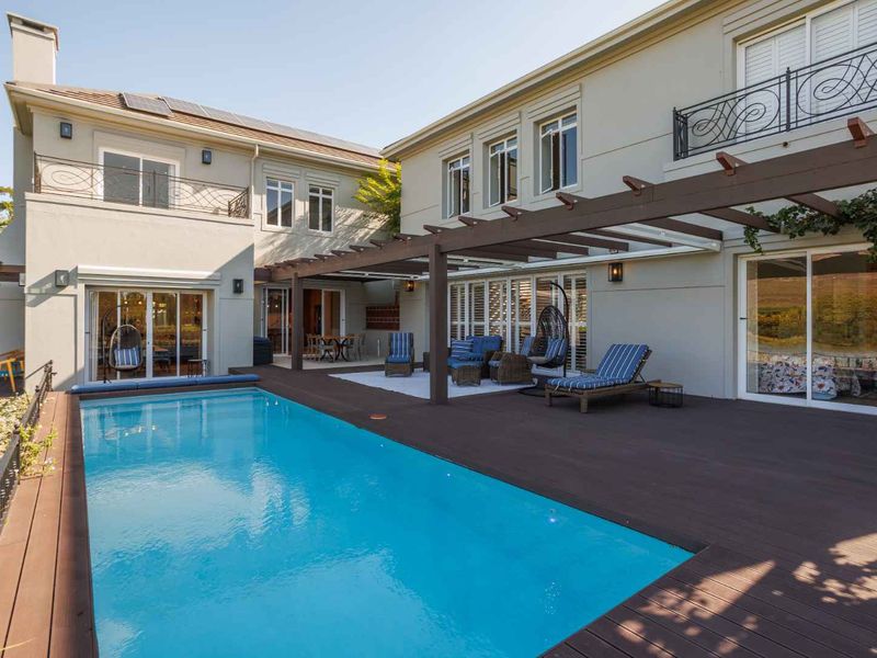 A well-maintained outdoor pool area featuring timber decking, a pergola, and direct access to the home through large sliding glass doors.