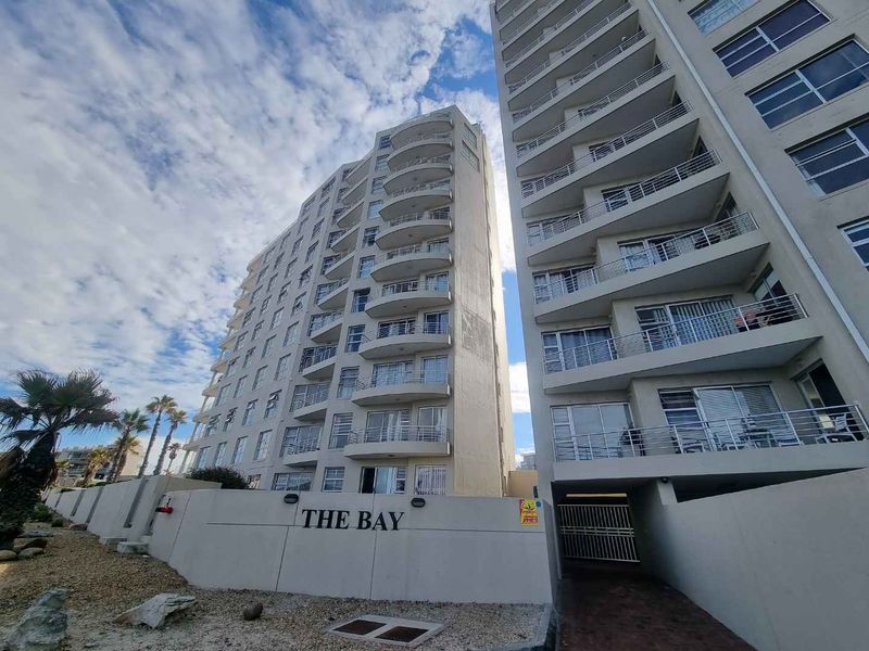 Exterior view of The Bay apartment complex featuring multi-story residential units with private balconies and a secure gated entrance.