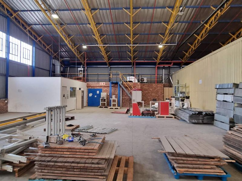 Spacious industrial warehouse featuring high-volume steel truss roofing, large windows for natural light, and functional open-plan floor space suitable for manufacturing or storage.