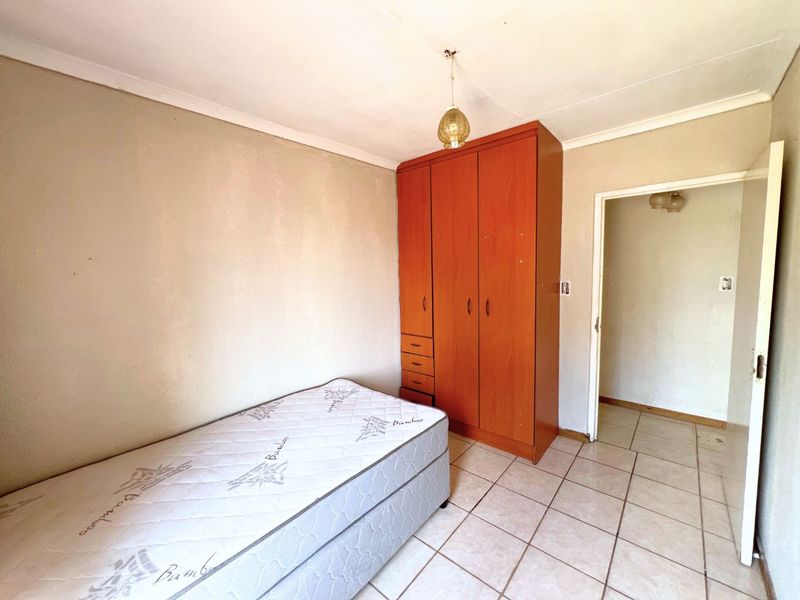 A bedroom featuring tiled flooring, a built-in wooden wardrobe, and a simple pendant light fixture.