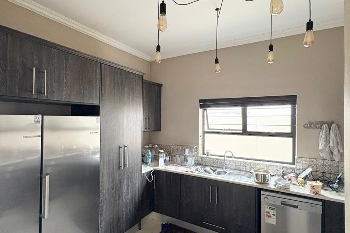 A functional kitchen featuring dark wood cabinetry, tiled flooring, a double sink, and a modern multi-pendant light fixture.