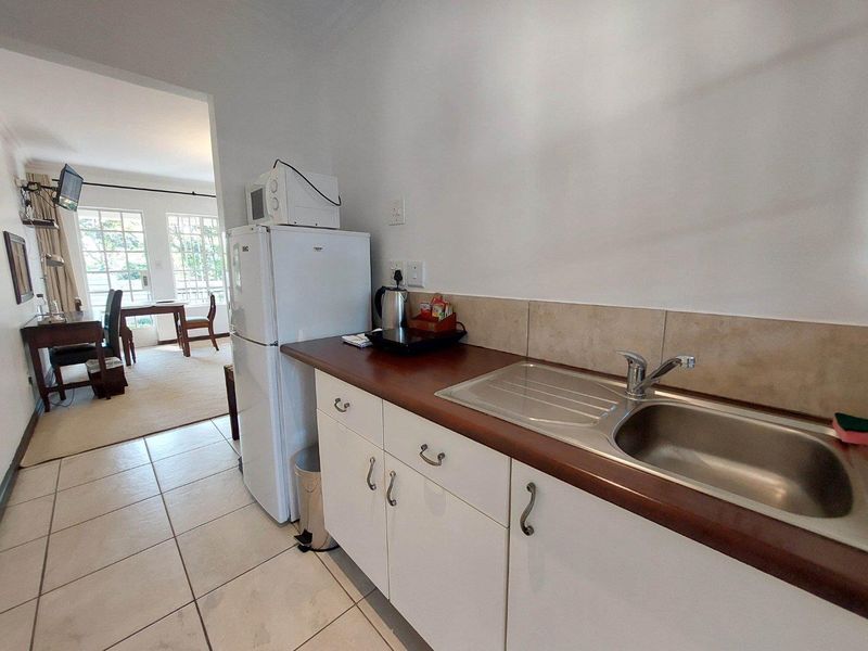 A functional kitchen area featuring white cabinetry, a stainless steel sink, tiled backsplash, and laminate countertops, with an adjacent dining space visible.