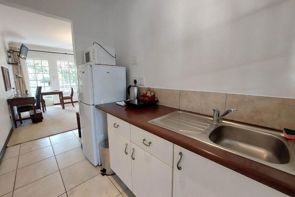 A functional kitchen area featuring white cabinetry, a stainless steel sink, tiled backsplash, and laminate countertops, with an adjacent dining space visible.