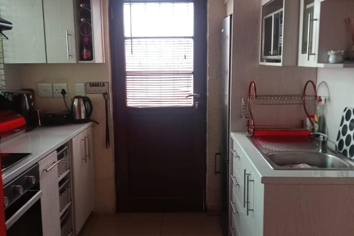 A functional galley-style kitchen featuring built-in cabinetry, integrated oven and hob, stainless steel sink, and direct access to an exterior door.