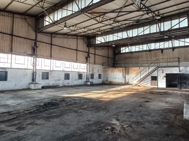 Spacious industrial warehouse featuring high ceilings, exposed steel trusses, large clerestory windows, and a concrete floor, suitable for manufacturing or storage operations.