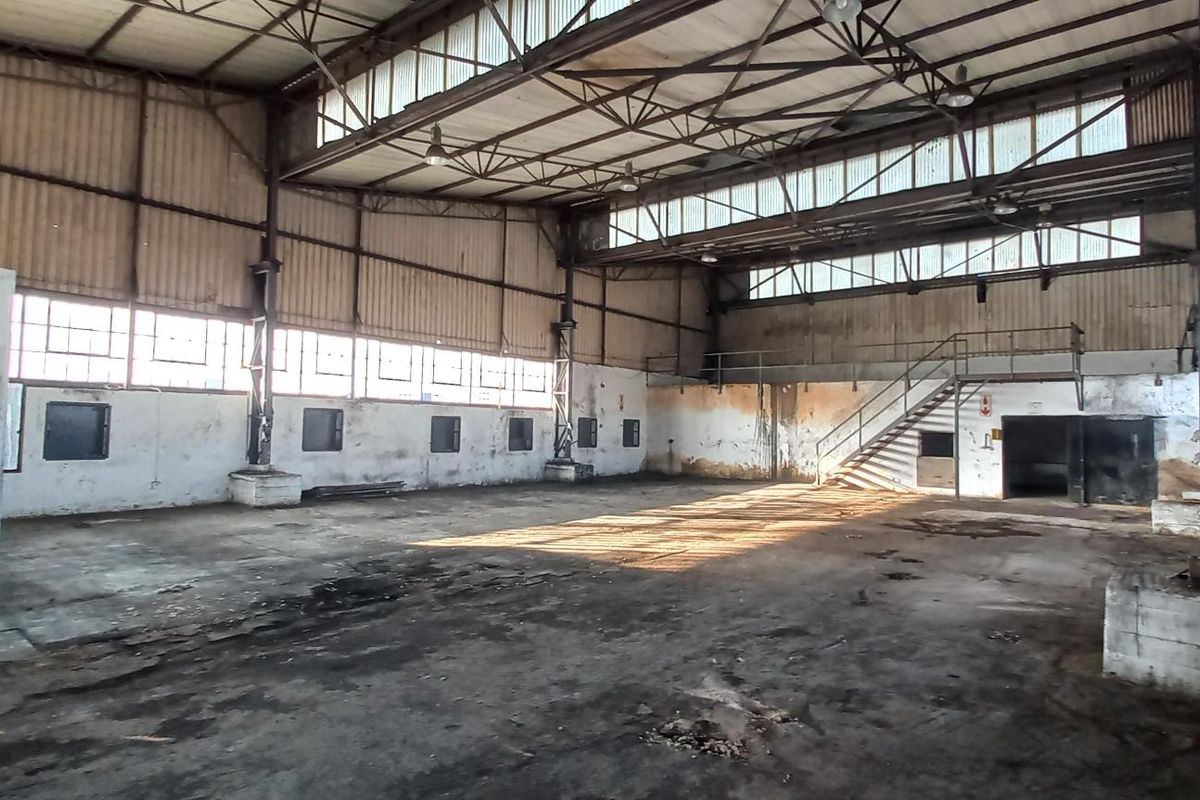 Spacious industrial warehouse featuring high ceilings, exposed steel trusses, large clerestory windows, and a concrete floor, suitable for manufacturing or storage operations.
