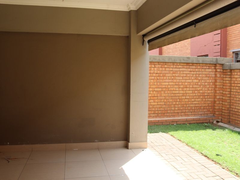 A covered patio area featuring tiled flooring, a retractable awning, and direct access to a small private garden with a brick boundary wall.