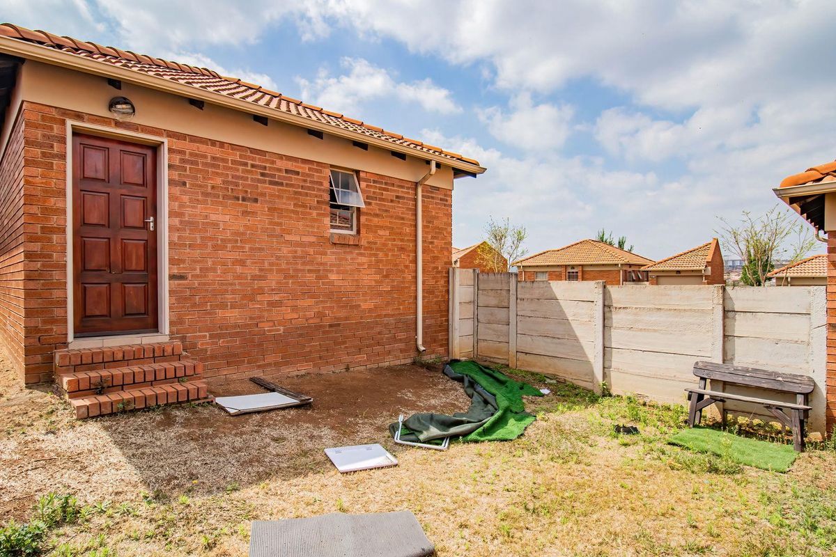 Rear view of a brick house featuring a tiled roof, timber door, and a private backyard area enclosed by precast concrete boundary walls.