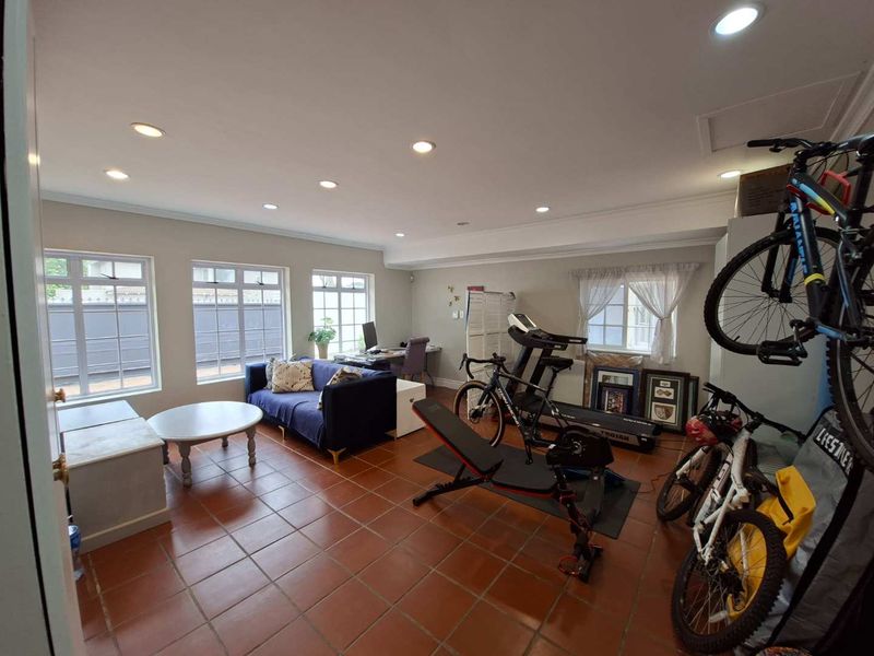 A spacious living area featuring terracotta floor tiles, recessed downlighting, and large multi-pane windows providing ample natural light.
