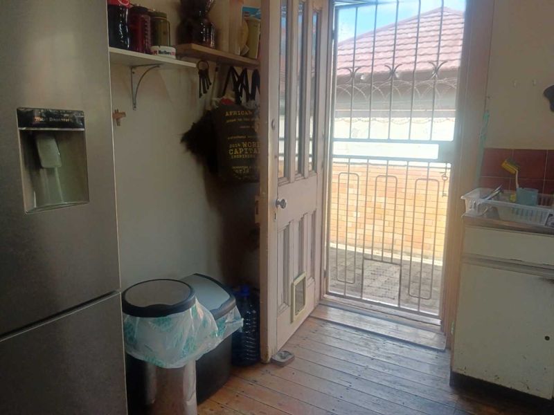 A functional scullery or utility area featuring timber flooring, a security gate leading outdoors, and tiled splashbacks, offering potential for modernization.