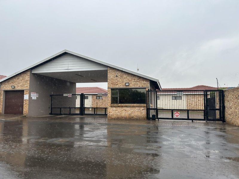Front entrance view of the townhouse complex featuring a brick security gatehouse, automated access gates, and perimeter electric fencing.