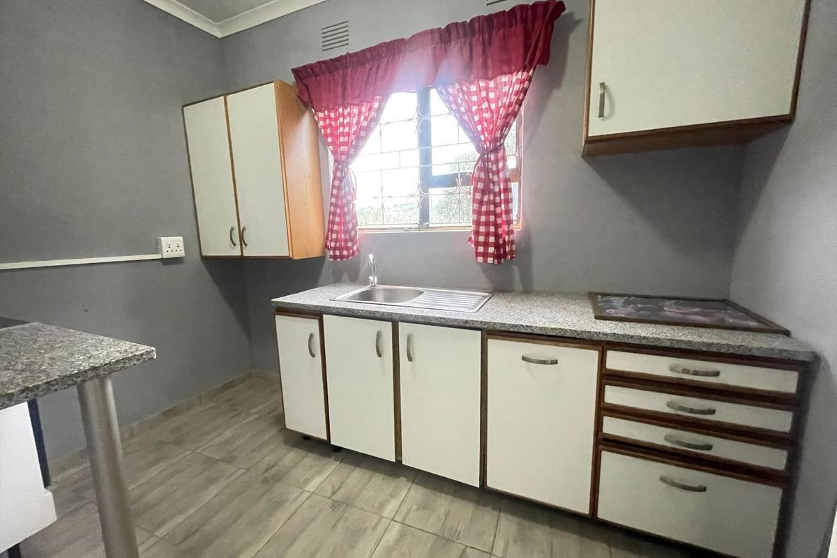 A functional kitchen featuring built-in cabinetry, laminate countertops, a stainless steel sink, and tiled flooring with security bars on the window.