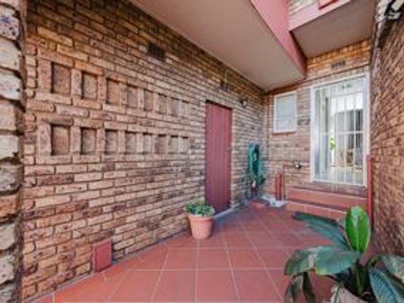 A covered outdoor patio area featuring face brick walls and tiled flooring, providing a functional transition space between the exterior and the home interior.