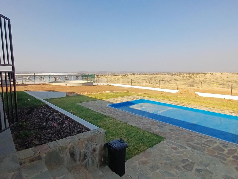 Outdoor pool area featuring a stone-paved patio, lawn, and perimeter fencing with expansive views of the surrounding landscape.