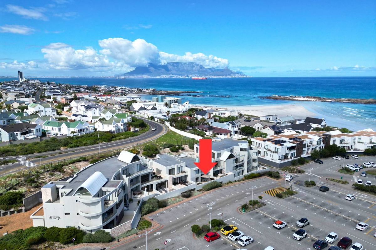 Aerial view of the apartment complex located near the coastline, featuring proximity to the beach and scenic mountain views.