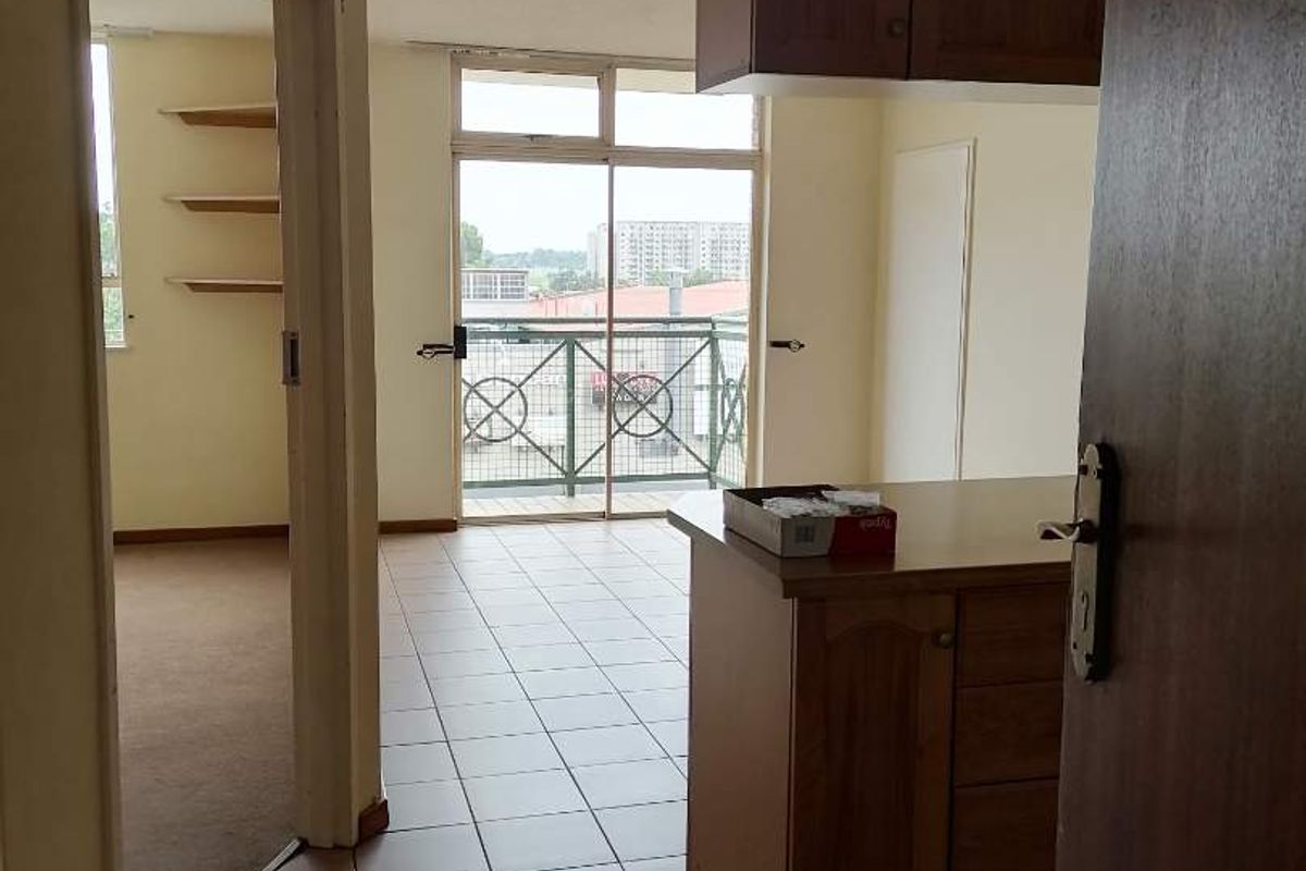 An open-plan living area featuring tiled floors, built-in kitchen cabinetry, and a sliding glass door leading to a balcony with metal railings.