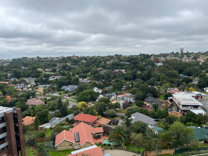 An elevated, wide-angle view overlooking a suburban residential neighborhood with lush greenery and various housing structures under a cloudy sky.