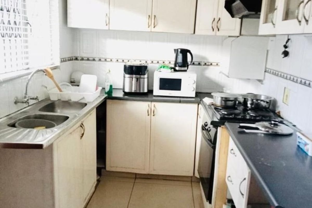 A functional kitchen featuring built-in cabinetry, a double bowl sink, and integrated cooking appliances, currently showing signs of wear and requiring cosmetic updates.