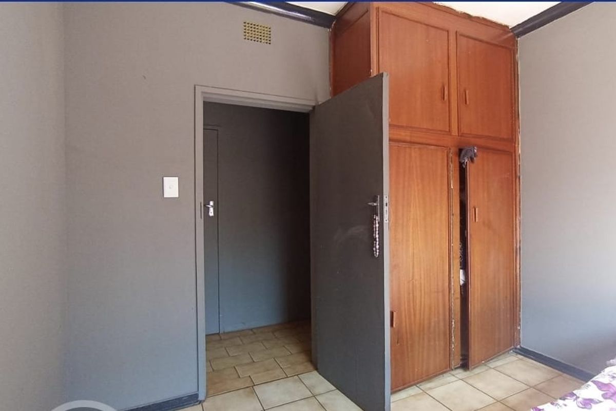 A bedroom featuring built-in wooden cupboards and tiled flooring, with a doorway leading to an adjacent space.