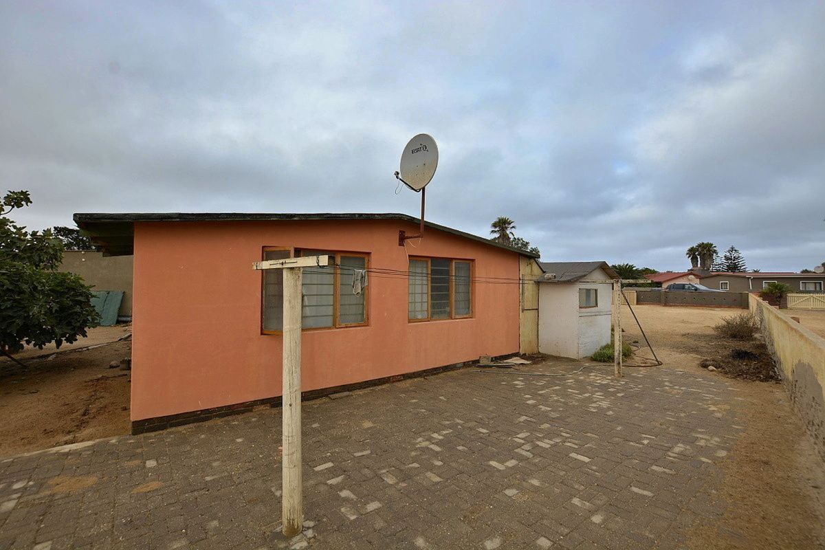 Rear exterior view of the property featuring a paved courtyard, satellite dish, and a small detached utility structure.