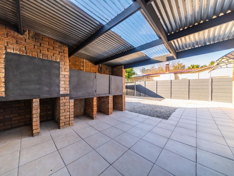 Covered outdoor patio area featuring a built-in brick braai, tiled flooring, and a corrugated roof, providing a functional space for outdoor entertaining.