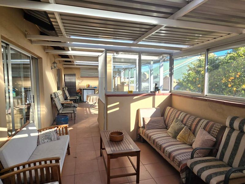 A covered patio area featuring tiled flooring, a metal roof structure, and large glass windows, providing a versatile outdoor living space.