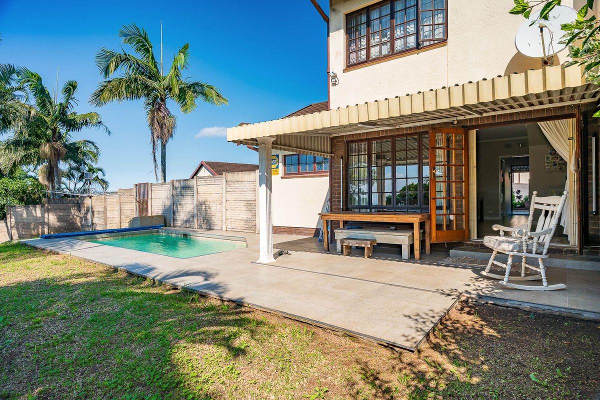 Rear exterior view featuring a swimming pool, paved patio area with a covered awning, and a fenced garden space.